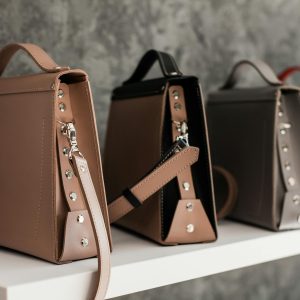 Luxury leather handbags displayed on a white shelf, showcasing minimalistic design and various colors.